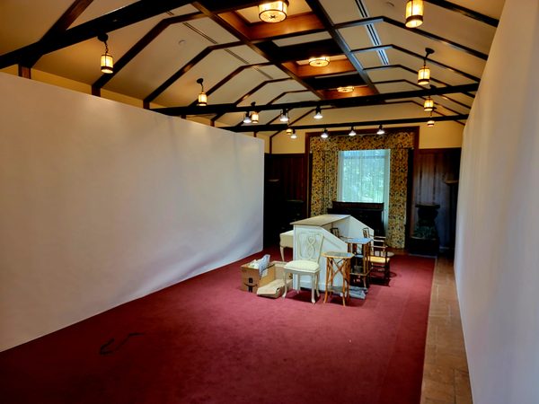Two tall white temporary walls over a red rug with a white chair and small tables in a room with a beamed wooden ceiling, Omaha 2023
